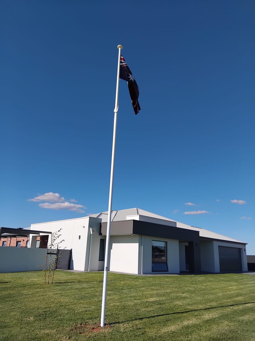 An Australian flag flying on a residential flagpole in a front garden